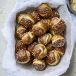 Sourdough Discard Pretzel Bites 5 Sourdough discard pretzel bites on a wooden board with a small bowl of dipping sauce, golden brown and sprinkled with coarse salt