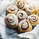 Sourdough Cinnamon Rolls Recipe 8 Golden-brown sourdough cinnamon rolls topped with creamy icing, arranged invitingly on a rustic wooden board.