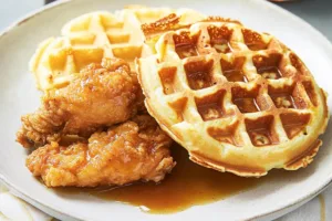 Homemade chicken and waffles topped with syrup and butter on a rustic wooden table
