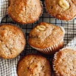 Sourdough Discard Banana Muffins 8 Freshly baked sourdough discard banana muffins on a cooling rack, golden brown and topped with walnuts.