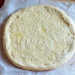 Sourdough Discard Pizza Dough 5 Golden-brown pizza crust made from sourdough discard, topped with fresh basil, tomato sauce, and melted cheese.