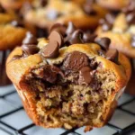Sourdough Discard Banana Chocolate Chip Muffins 8 Sourdough discard banana chocolate chip muffins on a wooden kitchen table, topped with melted chocolate chips and banana slices.