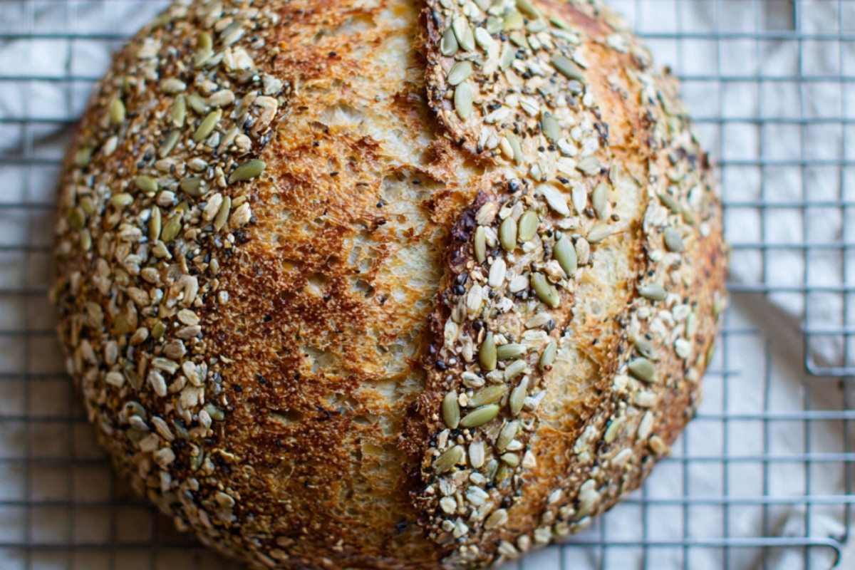 Freshly baked seeded multigrain sourdough bread loaf with a golden crust and hearty texture, displayed on a rustic wooden table.