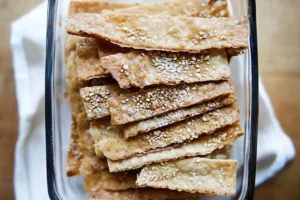 Crispy homemade sourdough discard crackers with herbs and sea salt, displayed on a wooden board with a rustic texture.