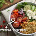 Mediterranean power bowl with quinoa, roasted chickpeas, cherry tomatoes, cucumber, olives, and feta cheese on a rustic wooden table