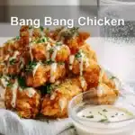 Bang Bang Chicken golden crispy pieces drizzled with sauce and fresh herbs on white cloth