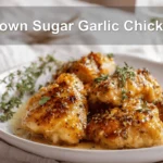 Brown Sugar Garlic Chicken plated with herbs, warm tones, and water glass on white napkin.