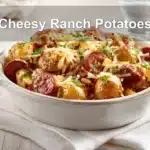 Cheesy Ranch Potatoes served with smoked sausage on white napkin, garnished with melted cheese and herbs.