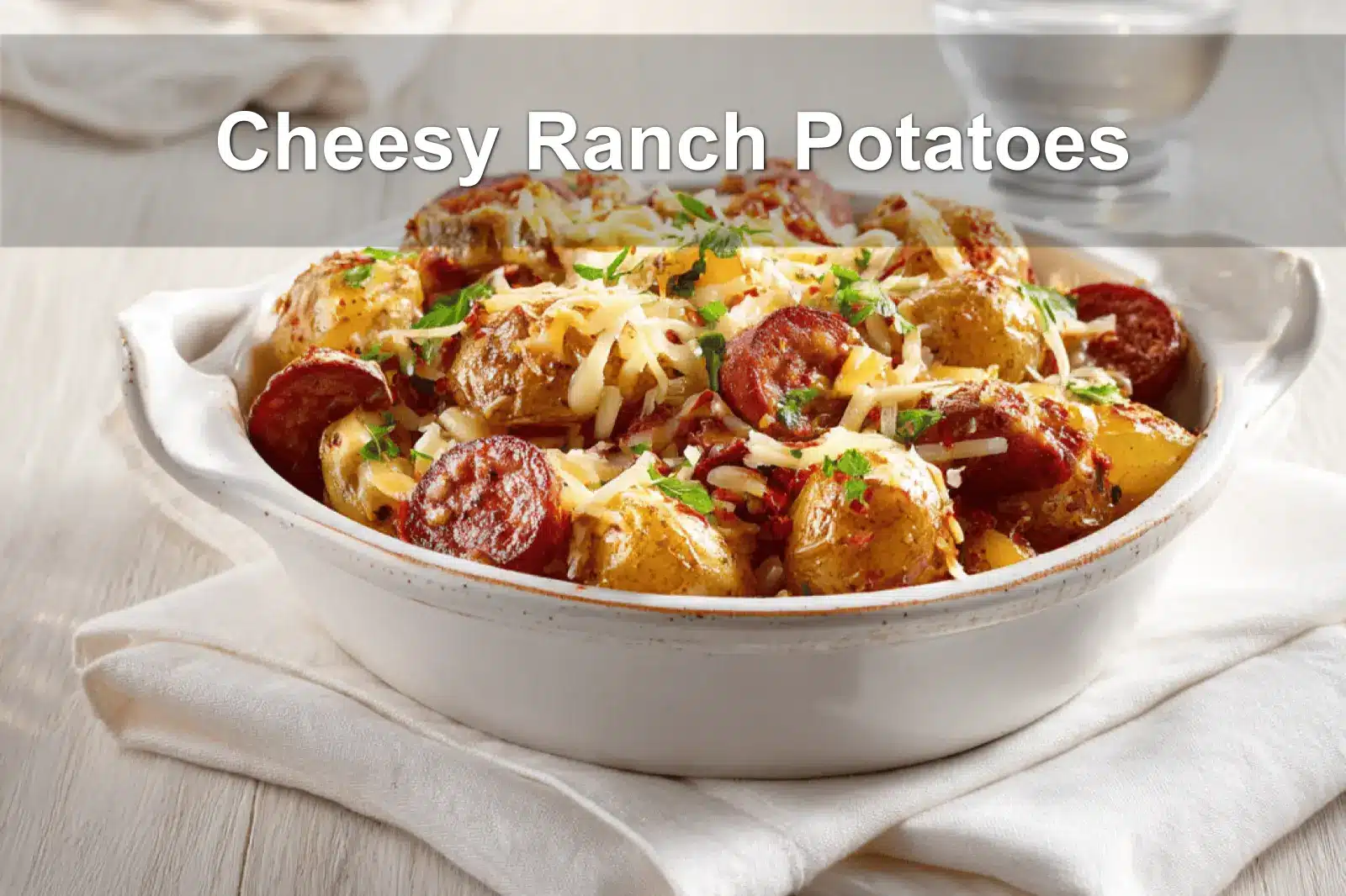 Cheesy Ranch Potatoes served with smoked sausage on white napkin, garnished with melted cheese and herbs.