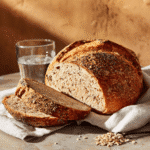 Sliced seed-packed protein sourdough bread on a white napkin with a glass of water beside it.