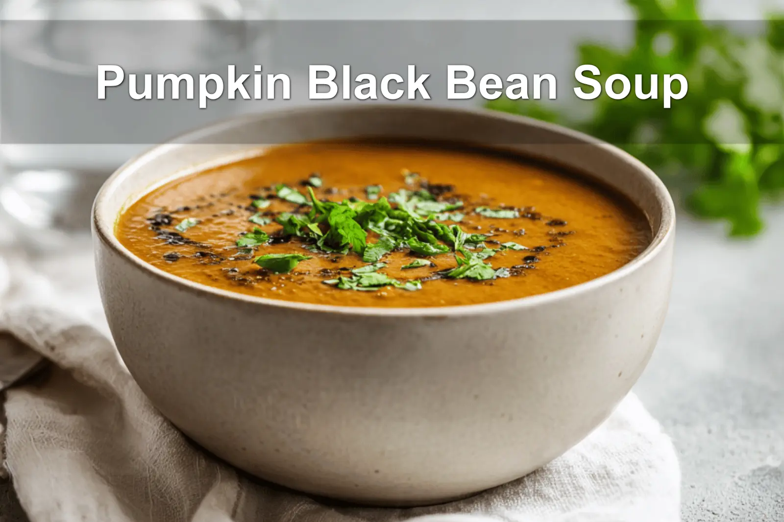 Pumpkin Black Bean Soup garnished with fresh herbs, served on a white napkin with a glass of water.
