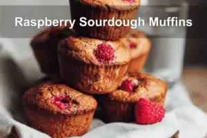 Raspberry sourdough discard muffins stacked on napkin beside water glass.