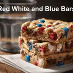 Freshly baked Red White and Blue M&M Cookie Bars stacked on a white napkin with natural lighting.