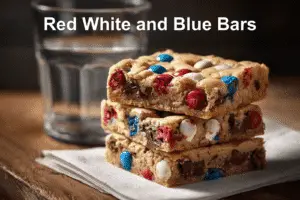 Freshly baked Red White and Blue M&M Cookie Bars stacked on a white napkin with natural lighting.