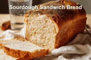 Sourdough sandwich bread loaf sliced to reveal fluffy interior on a white napkin.