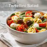Vibrant tortellini pasta salad with fresh ingredients served in a white bowl, glass of water on the side.
