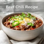 Beef Chili Recipe hearty bowl with shredded cheese fresh herbs jalapeños on white napkin
