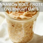 CINNAMON ROLL PROTEIN OVERNIGHT OATS jar with cinnamon swirl on white napkin beside water