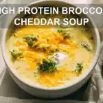HIGH PROTEIN BROCCOLI CHEDDAR SOUP creamy bowl on white cloth with clear glass of water