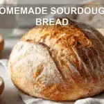 HOMEMADE SOURDOUGH BREAD golden crust loaf on white cloth with starter and glass of water