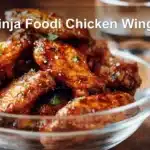 Ninja Foodi Chicken Wings on white napkin with clear glass of water and golden glaze