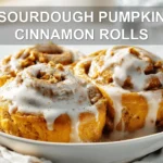 SOURDOUGH PUMPKIN CINNAMON ROLLS glazed rolls on white cloth with clear water glass
