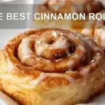 THE BEST CINNAMON ROLLS warm glazed pastries on white cloth with glass of water