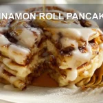 CINNAMON ROLL PANCAKES stacked with maple syrup and delicate white cheese glaze on white cloth