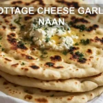 COTTAGE CHEESE GARLIC NAAN warm golden flatbreads on white napkin with a clear glass of water