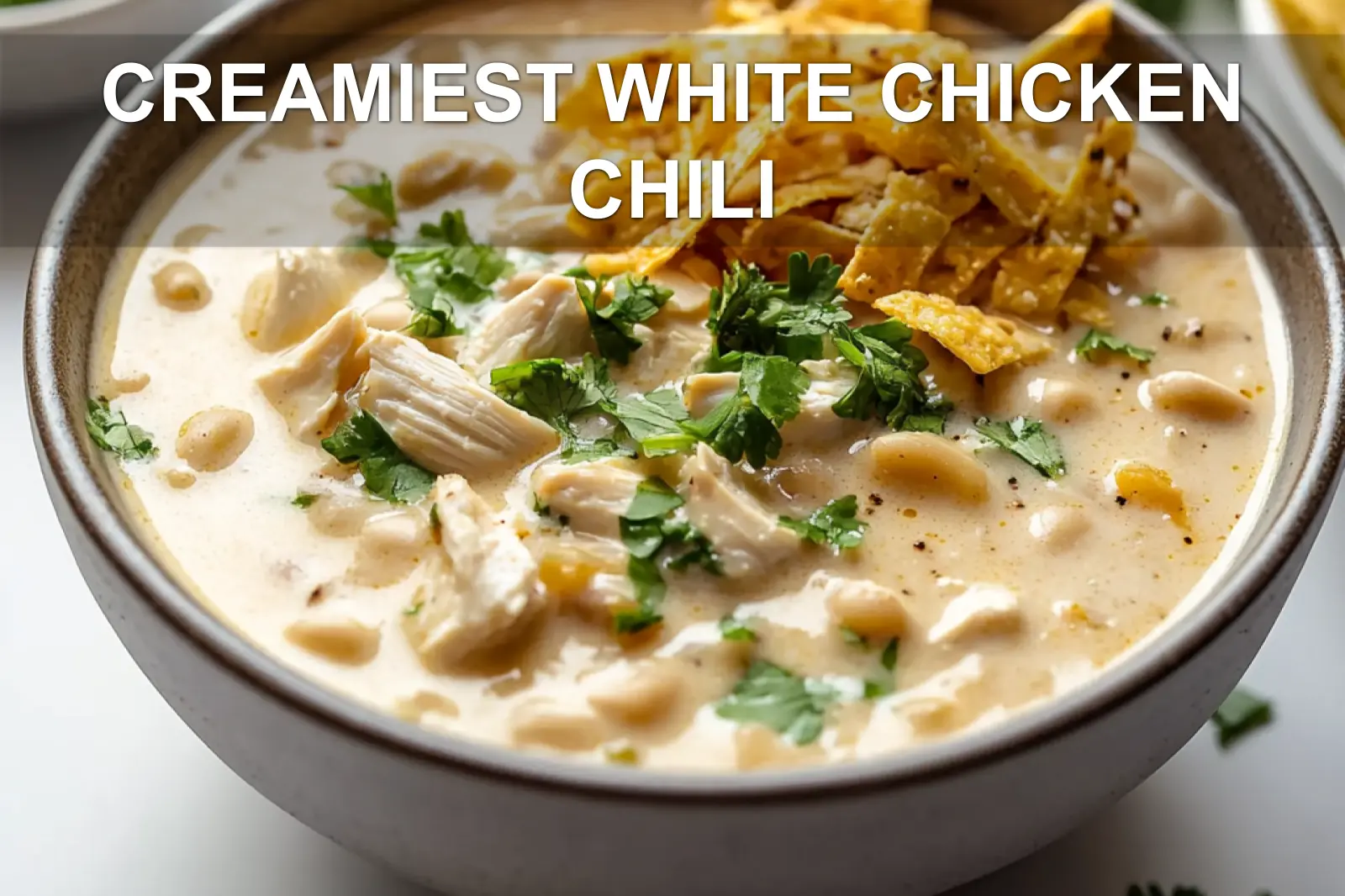 Extra creamy white chicken chili in a bowl with shredded cheese, cilantro, and a hint of lime, ready to serve
