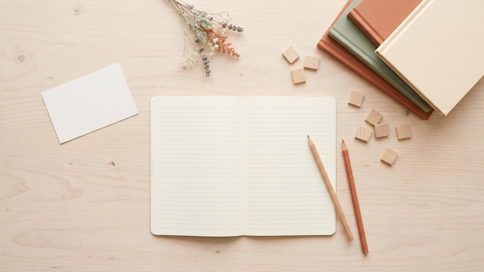 Homeschool Language Arts Curriculum: All-in-One or Separate Subjects? 2 Flat lay of an open lined notebook, pencils, books, wooden letter tiles and a blank card on a pale wooden table